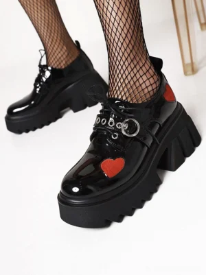 Black gothic lolita platform shoes with red heart accents, patent leather finish, side view showing serrated lug sole and round toe shape, worn with black fishnet stockings