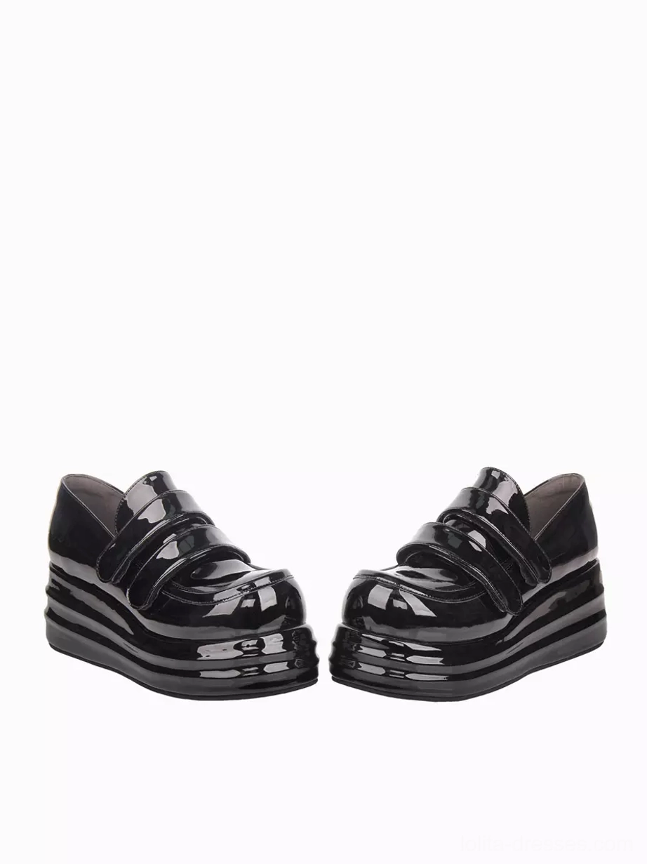 Side oblique angle of black glossy patent leather Lolita platform shoes showing high wedge sole and hook-and-loop strap fastening system