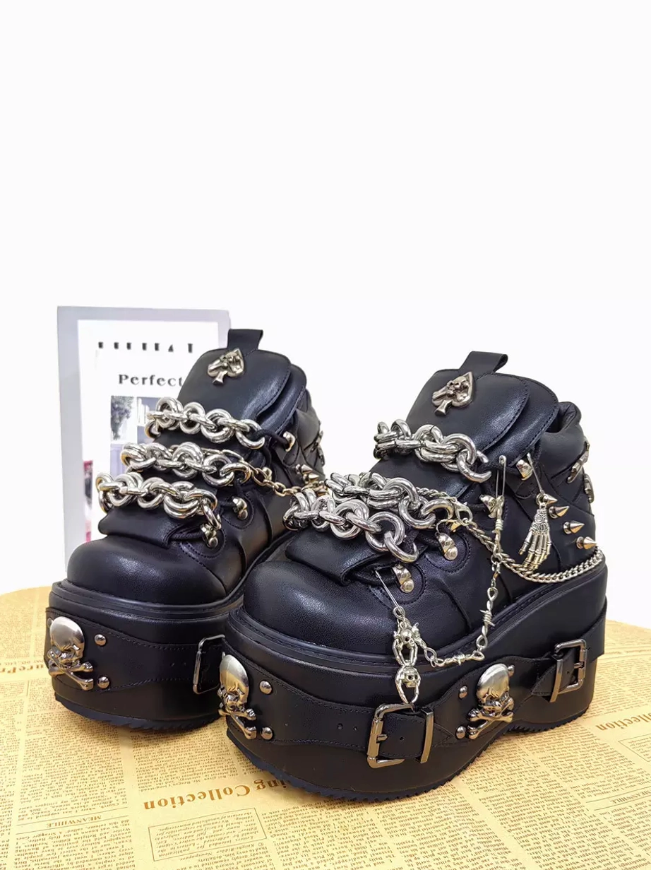 Pair of gothic lolita platform wedge shoes front three-quarter view newspaper background black pu leather spade tongue ornament skull platform buckles