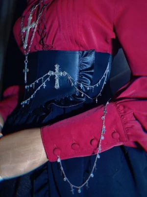 Gothic lolita black and dark blue PU leather waist chain corset with silver cross pendant chains worn over ruffled red cuffs close-up detail view