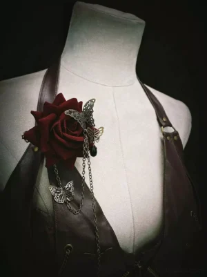 Close-up front view of Gothic rose chain brooch featuring deep red velvet rose silver butterfly pendants and long dangling chains on leather harness against off-white dress form