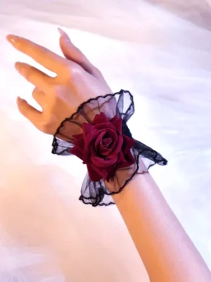 Single rose lace wrist cuff gothic lolita accessory close-up side view showing black ruffled mesh and wine red velvet rose detail on pink sheer fabric background