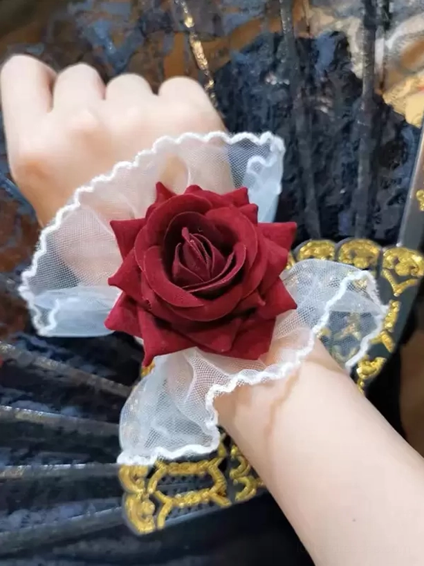 gothic lolita rose wrist cuff with black mesh ruffle trim and burgundy fabric rose, worn on single wrist against dark gold-trimmed folding fan background, close-up detail view