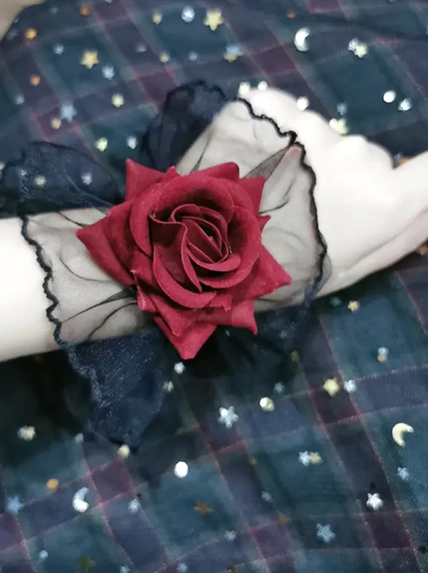 pair of matching gothic lolita rose wrist cuffs on two wrists, top-down perspective showing black sheer mesh trim and burgundy rose details against plaid star-moon printed fabric backdrop