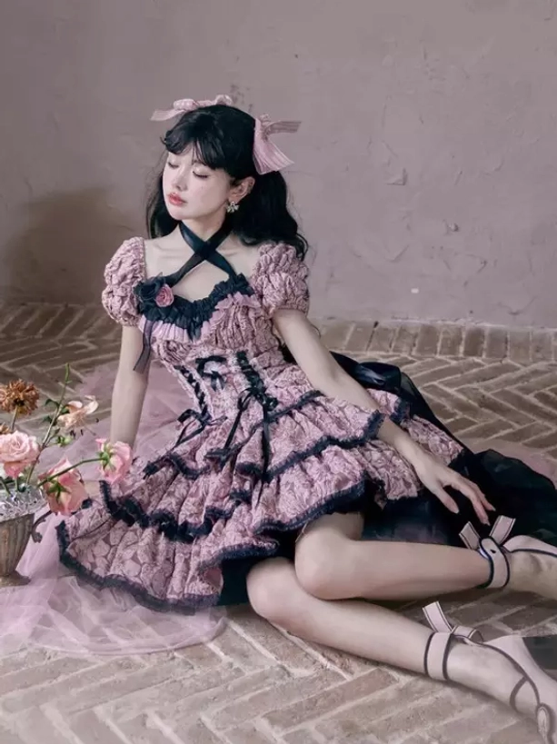 Pink Gothic Lolita dress with tiered ruffled skirt layers, trailing black sash, ankle strap platform heels, pink head bow, brick floor interior scene