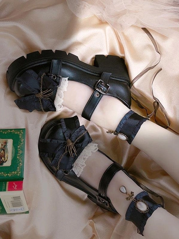 Black gothic Lolita platform shoes side view worn on feet with pearl-decorated ankle cuffs, skeleton hand bow ornament, and block heel on vintage card backdrop
