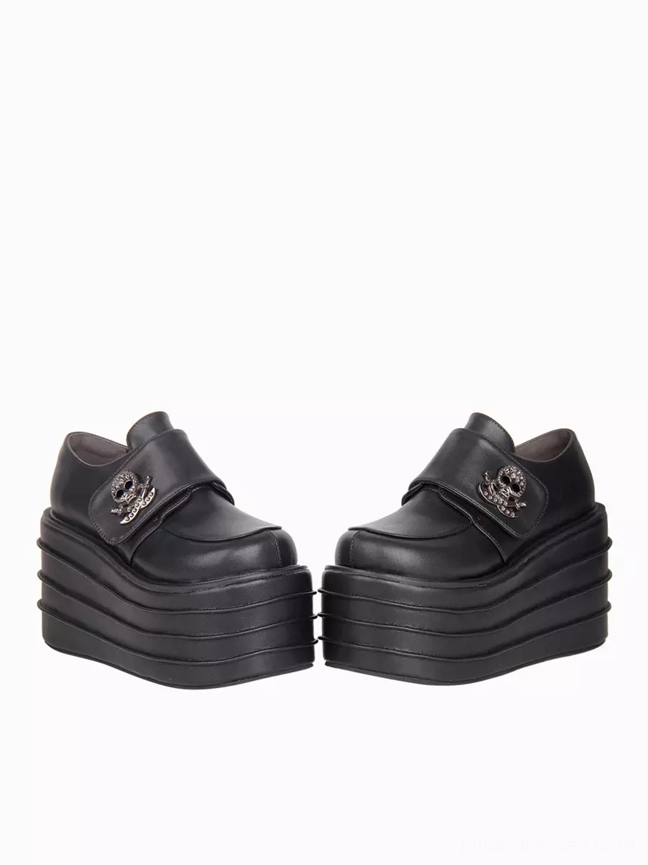 Gothic lolita platform shoes frontal flat view showcasing black PU leather upper, dual skull metal buckles, and thick multi-layered platform sole structure