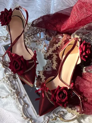 Red Gothic Lolita stiletto pumps with silk roses and gold chain trims, pointed toe, ankle strap, displayed on ornate vintage mirror with lace and pearl chains