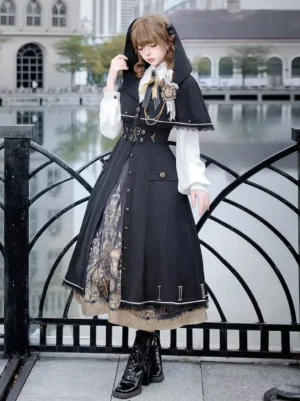 Black Gothic Lolita cape collar vest with white puff blouse and castle print skirt worn by female model at waterfront iron fence location with decorative brooch detail and capelet design
