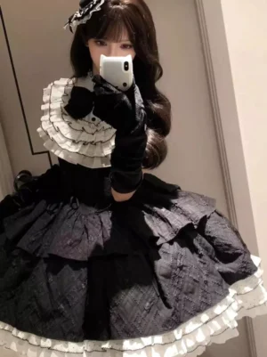 Gothic lolita tiered ruffle dress front view detail showcasing corset bodice structure, white ruffled collar layers, black bow accent, long black velvet gloves, and multi-layer quilted lace skirt hem against mirror background