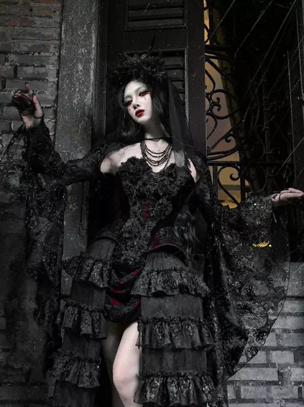 Gothic black and red lolita outfit with long lace sleeves and ruffled tiered skirt, half front angle showing model with dark headpiece against brick wall doorway entrance