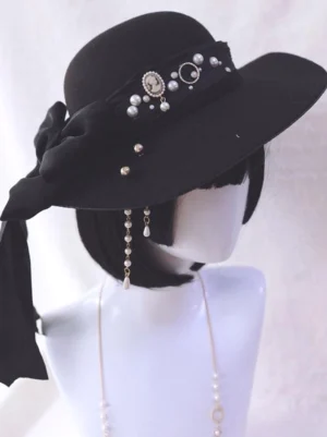 Gothic Lolita black wide-brim hat with pearl and chain embellishments, side view on display mannequin showing felt fabric, vintage metal trims, and decorative back bow with flowing ribbon