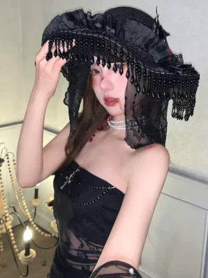 Gothic Lolita witch hat front close-up showing intricate black lace, drop bead tassel veil, red rose cross decoration, paired with pearl choker and strapless black lace dress