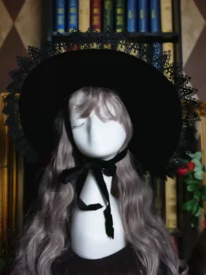 Black lolita witch hat front side angle view showing black ribbon chin strap and intricate lace detailing on mannequin with curly wig
