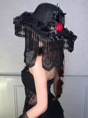 Gothic Lolita witch hat rear view featuring ruffled black lace brim, beaded fringe veil, red rose and cross ornament, black feather accent, worn by model in black lace dress