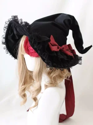 Dark red and black Gothic Lolita witch hat with lace trim, fabric roses, red satin ribbon, and eye patch detail - left three-quarter view on blonde curly wig mannequin