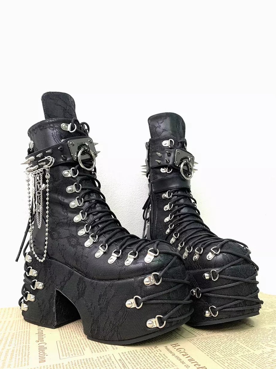 Gothic platform boots front three-quarter angle featuring silver hanging chain pendants spiked buckle strap lace-up metal eyelets and chunky wedge heel on newspaper background