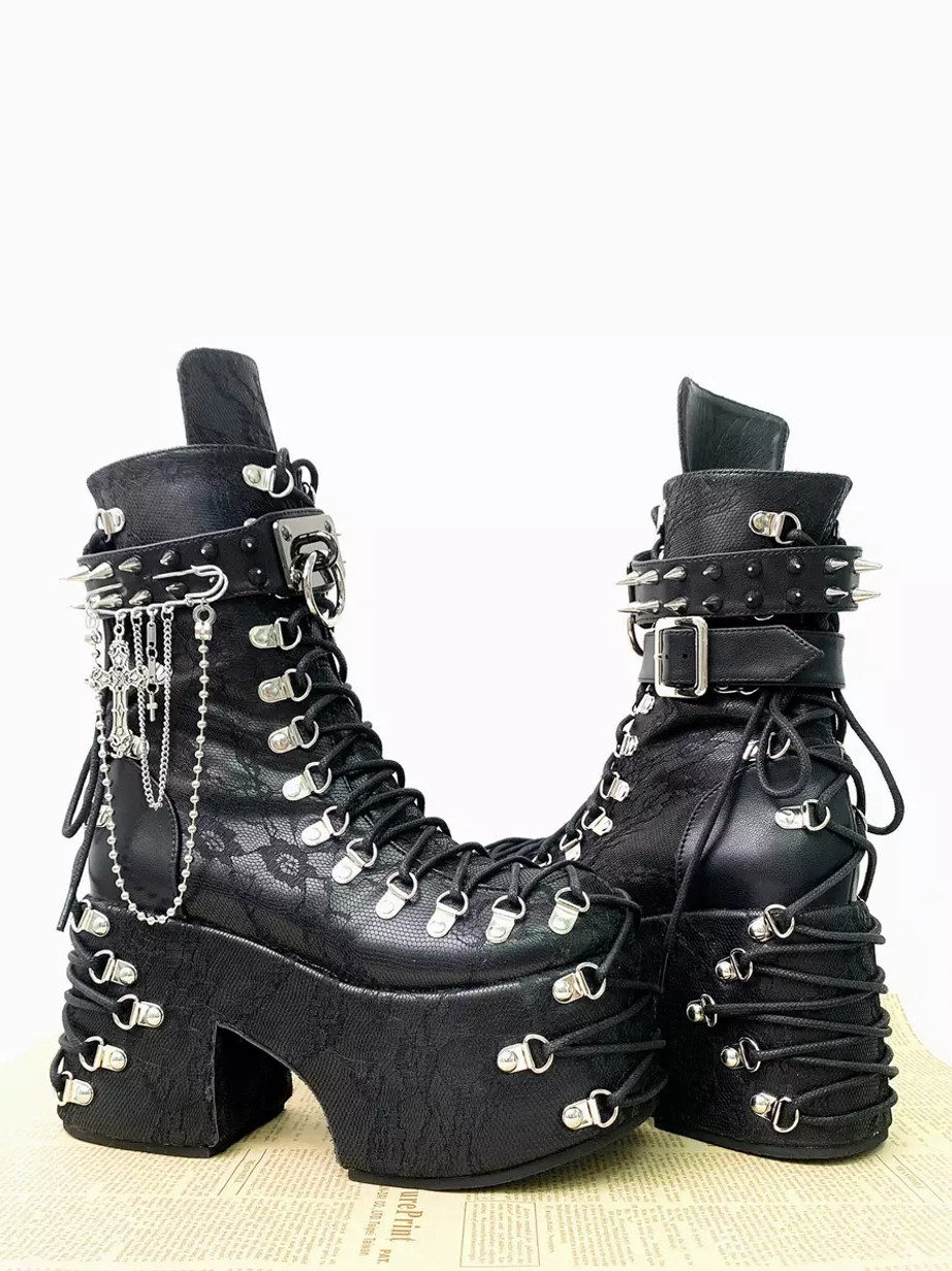 Front three-quarter view of gothic platform combat boots with safety pin and chain decorations spiked ankle strap embossed leather texture and thick sole on newspaper background