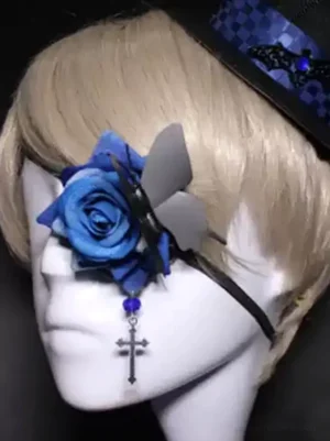 Gothic rose eye patch mask worn on mannequin head with ash blonde hair and checkered top hat, featuring blue fabric rose with black butterfly and silver cross charm, showcasing left side profile view with black velvet strap