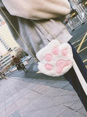 Gray and pink fuzzy cat paw crossbody bag with gold metal chain, side rear view on model wearing gray coat, soft plush texture and cute paw shape details clearly visible