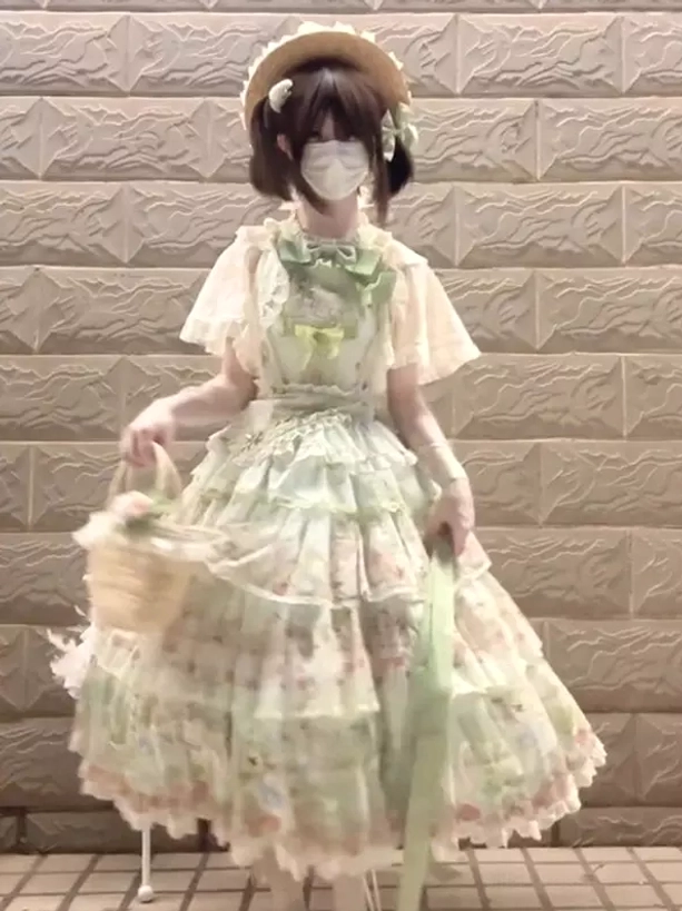 Side three-quarter view of green pastel floral gothic lolita JSK dress highlighting silhouette volume, coordinating long waist sash, model with flower basket accessory