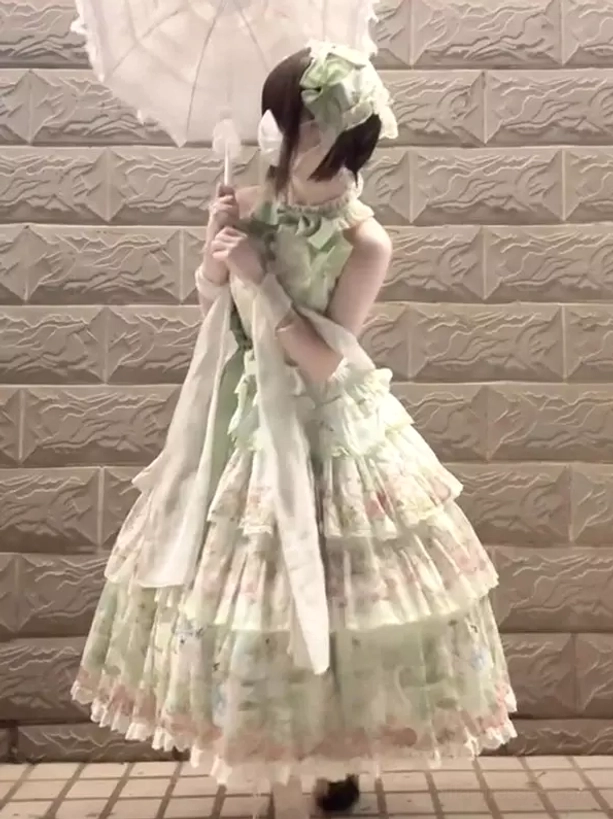 Back side view of green gothic lolita JSK dress showing halter neckline design, draped fabric sashes, white parasol accessory, flower hair ornament detail