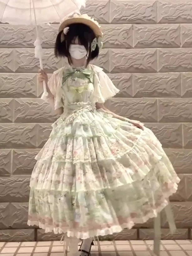 Gothic lolita green dress three-quarter front angle showing flared layered tiered skirt with lace trims, model holding white lace parasol, straw hat accessory