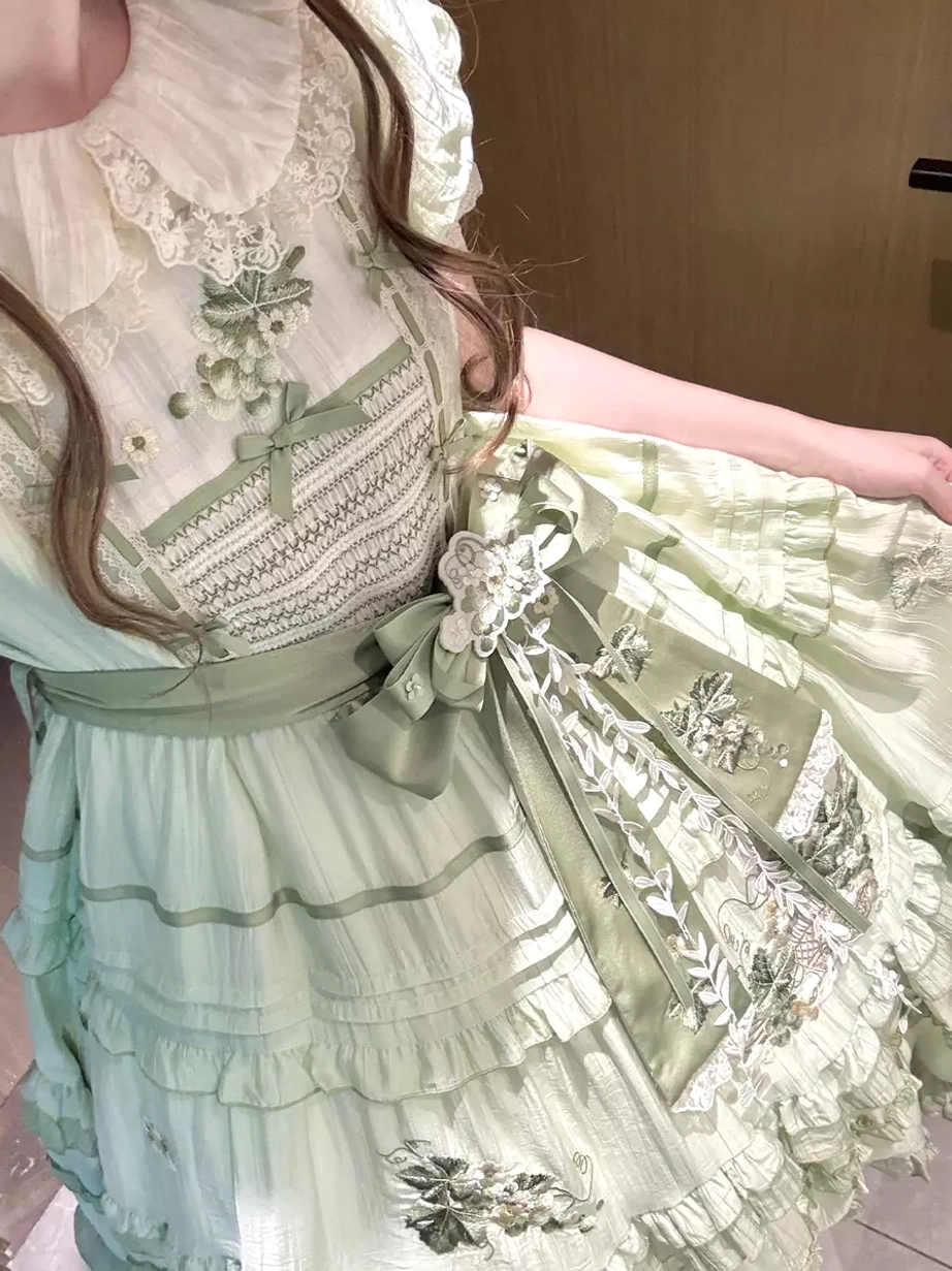 Close-up front detail view of green sweet lolita dress showing intricate floral embroidery pattern, Peter Pan collar with lace trim, waist sash bow, layered ruffled skirt construction