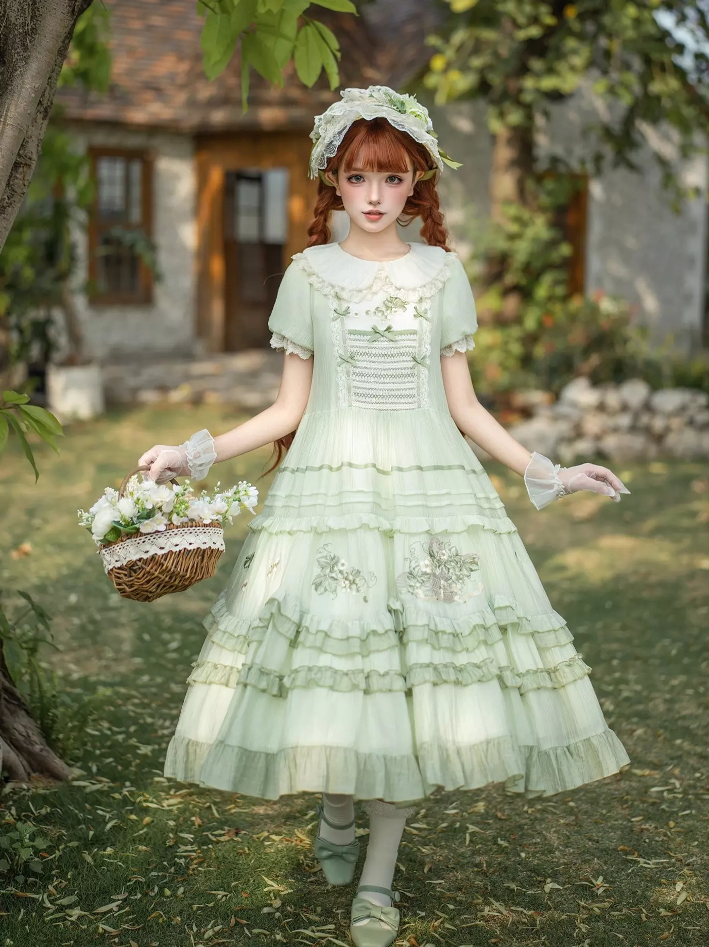 Full-body front view of model wearing green sweet lolita dress with matching bonnet, lace gloves, carrying decorative flower basket, outdoor yard scene with natural background