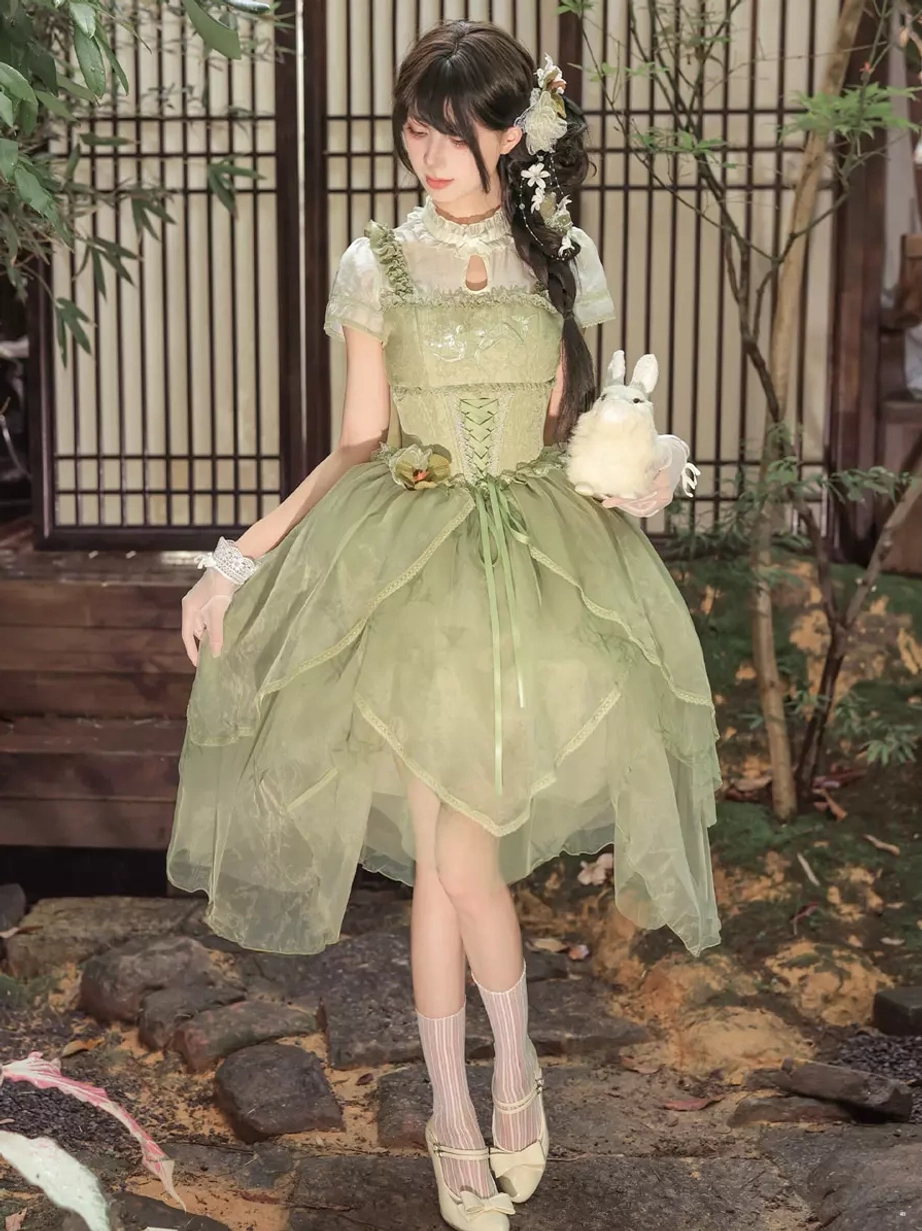 Green sweet lolita midi dress worn by model holding plush rabbit in traditional garden scene showing corset waist, layered tulle skirt, and short puff sleeve design