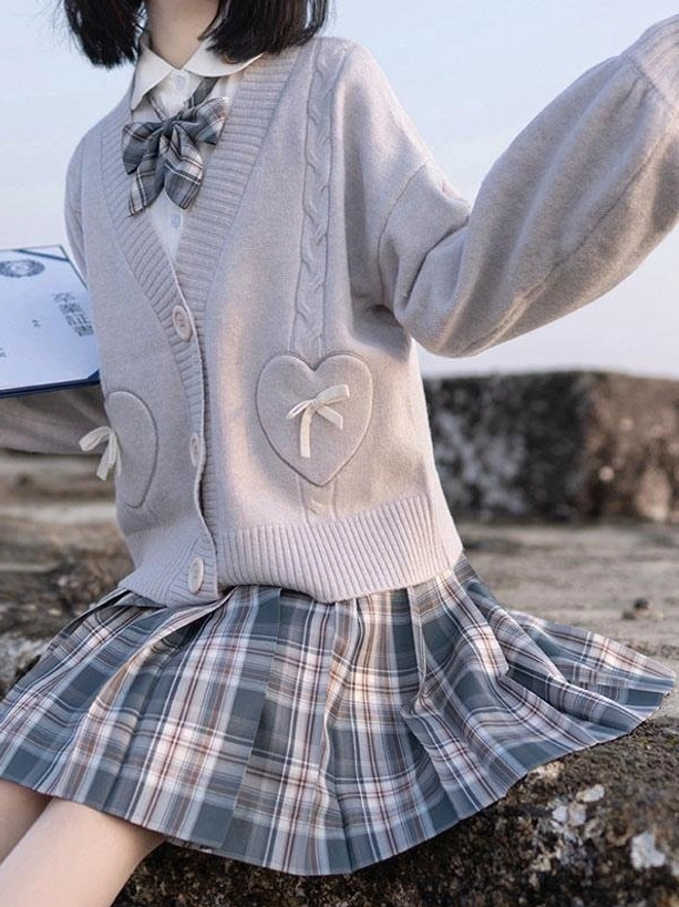 Light grey lolita sweater cardigan with plaid bow tie and heart bow pockets shown in side view on outdoor stone setting