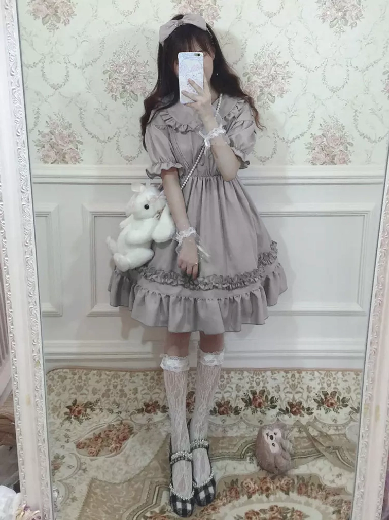 Grey Sweet Lolita OP dress with ruffled Peter Pan collar worn by model in side view, showcasing short puff sleeves and layered ruffled skirt with hair bow accessory in vintage floral room setting