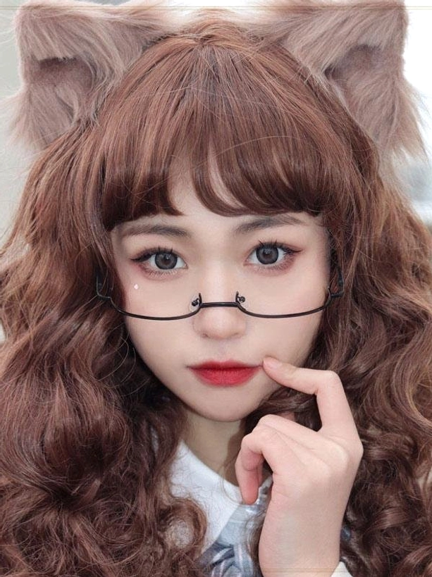 Close-up portrait featuring model in lolita coordinate with black half-frame glasses, fluffy cat ears hair accessory, and brown curly wig, hand posed near chin showcasing complete accessory layering
