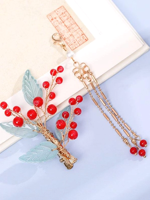 Close-up flat lay of individual Hanfu hair accessory hairpin with red bead clusters, frosted blue leaves, gold metal wiring, long flowing gold tassel chain with red bead terminal ends on vintage background