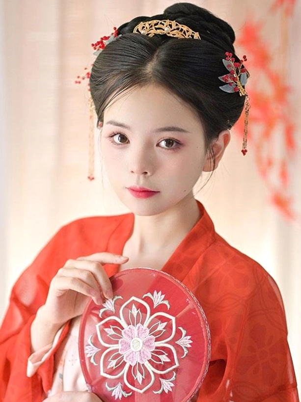 Front-facing portrait of woman in red Hanfu holding embroidered round fan, displaying full view of gold hair comb, side hairpins with red berries, tassels and chain ornaments