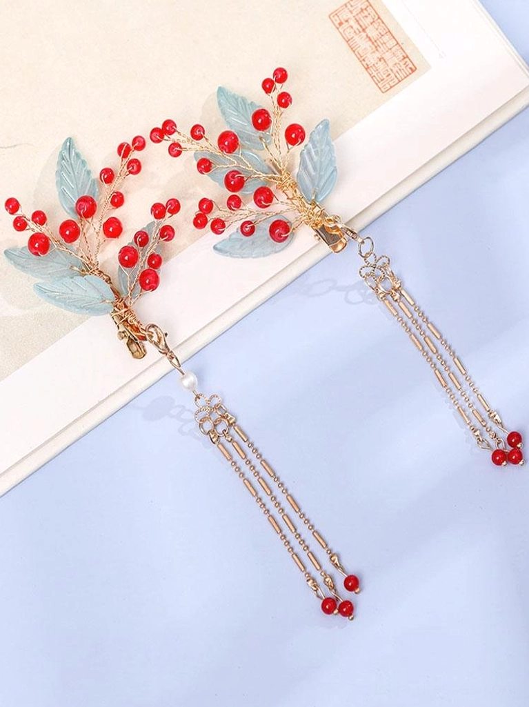 Flat lay detail of single Hanfu hairpin with double gold chain tassels, red bead berries, frosted light blue resin leaves, gold metal hardware, and white pearl accents on vintage paper background