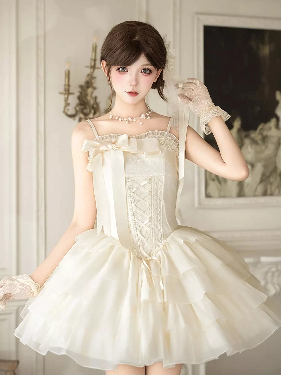 Full front view of ivory spaghetti strap corset Lolita mini dress featuring dramatic tiered ruffled tulle skirt and oversized front bow in vintage European room