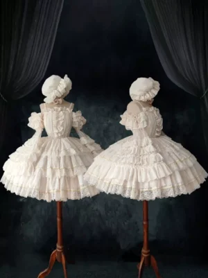 Two matching ivory sweet Lolita wedding dresses displayed together on dress forms, showcasing the voluminous ruffled skirts with gold trim and coordinating bonnets