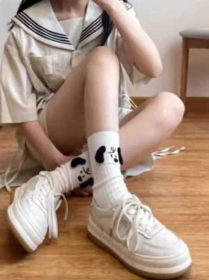 Sweet lolita socks featuring ribbed knit fabric with black puppy embroidery details, side seated view of model adjusting socks in sailor collar dress style