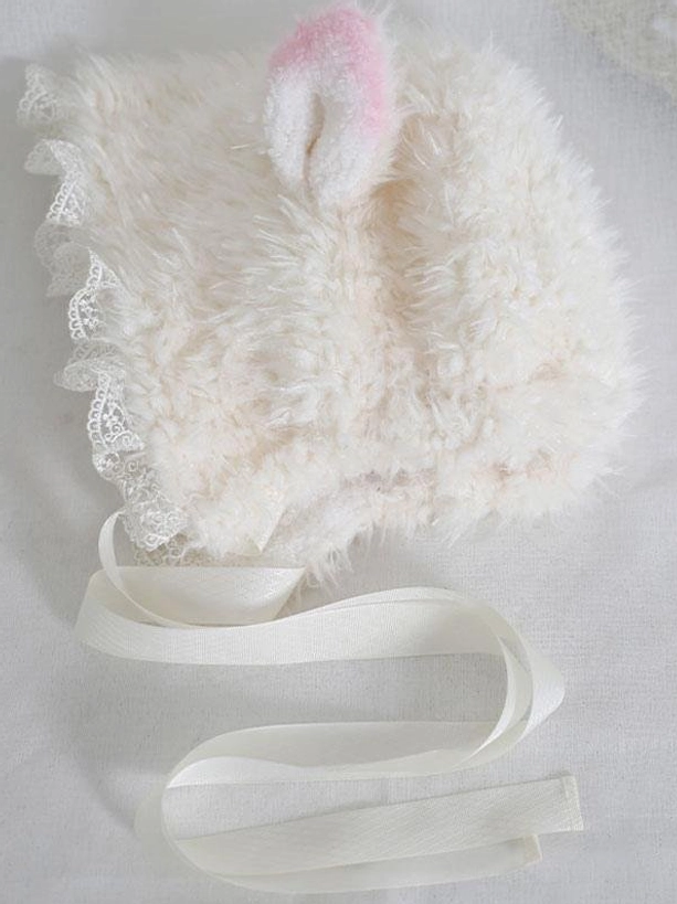 Side flat lay view of lamb ear bonnet displaying single pink-ombre ear plush texture and adjustable satin neck ribbons