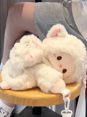 Two matching lamb plush crossbody bags in white and pink with bow decoration displayed on wooden stool top-down view