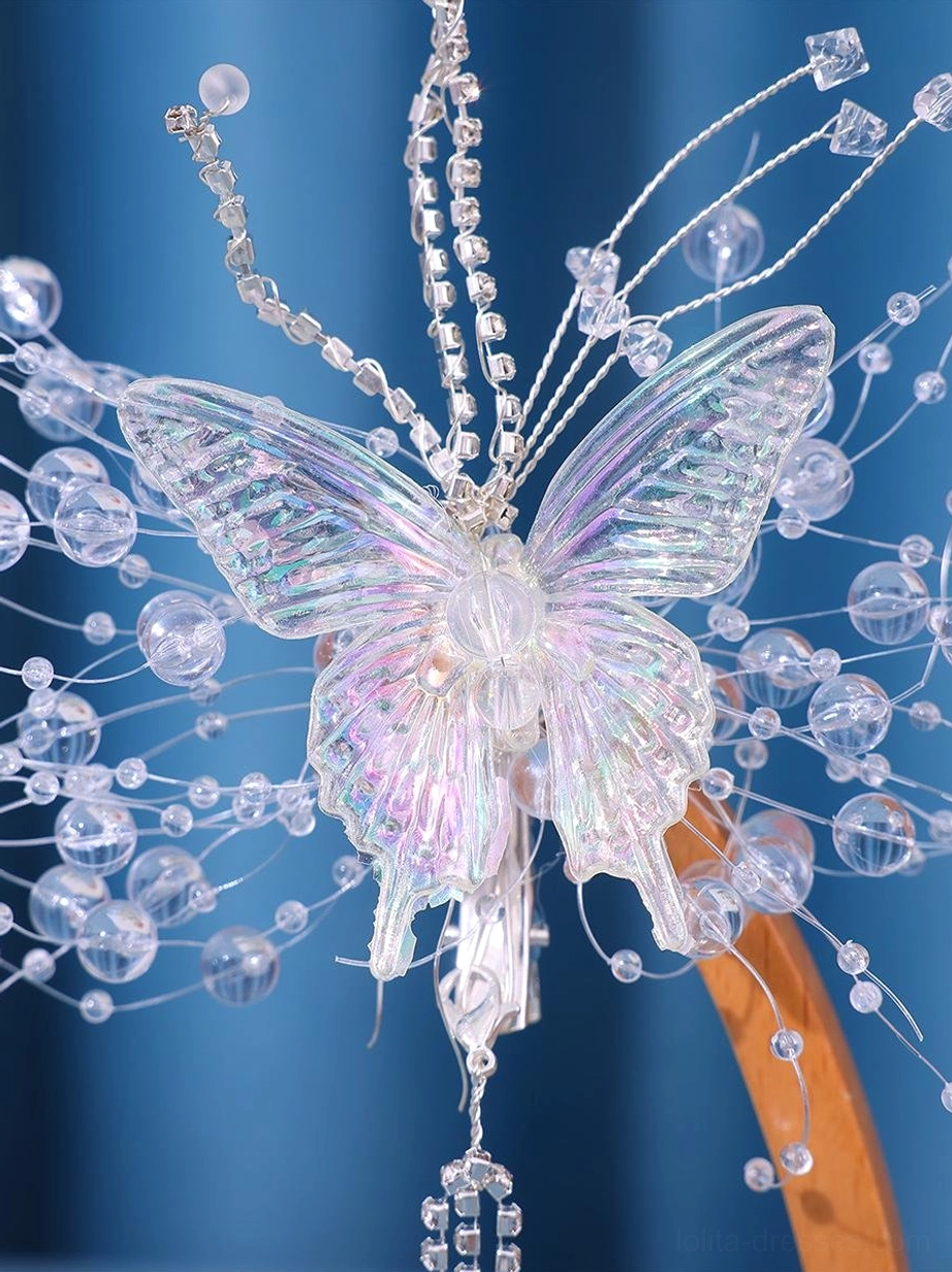 Large iridescent butterfly hairpiece close-up flat lay on blue background showing crystal wire fringe and cascading rhinestone chain tassel