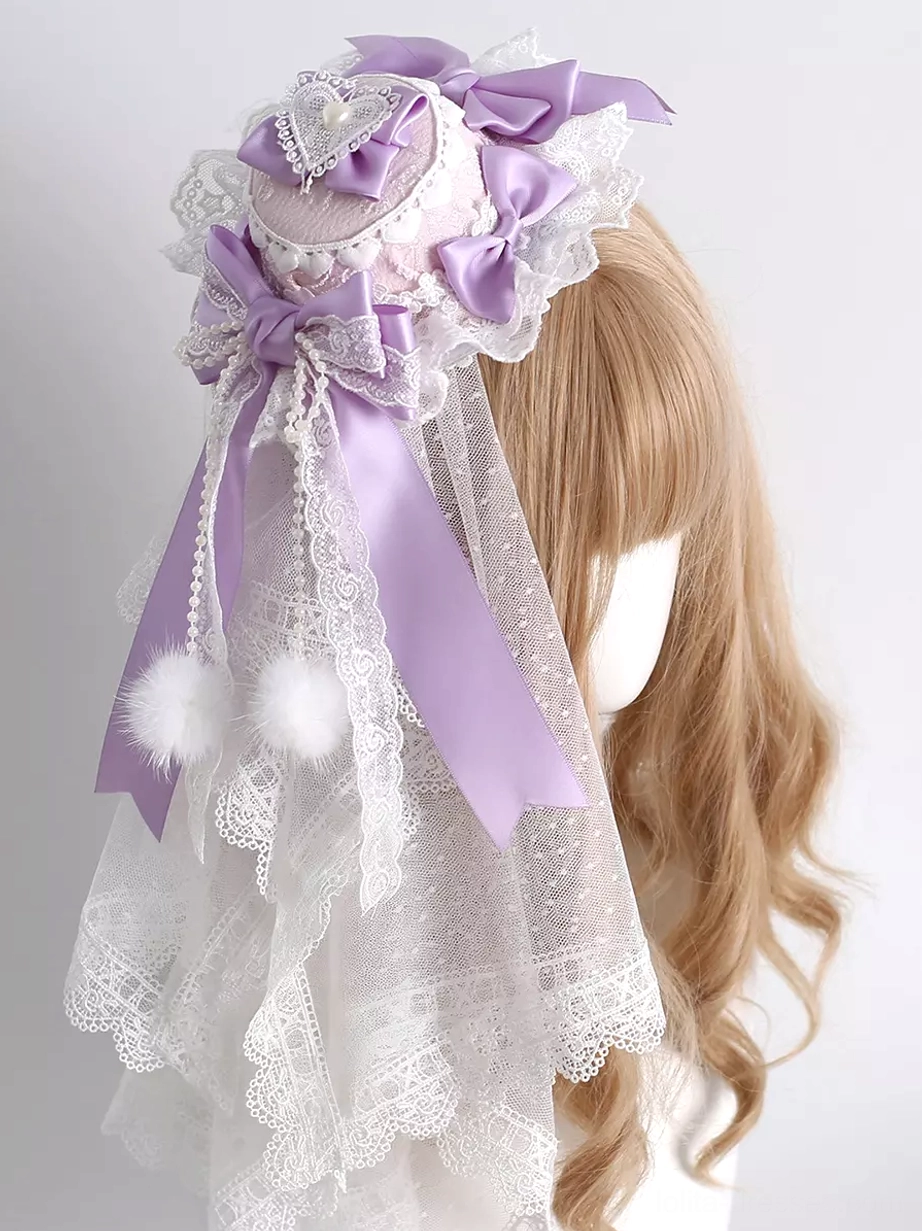 Lavender sweet lolita mini top hat hair clip with white lace trim and purple satin bows featuring fluffy pom-poms and heart rhinestone decorations displayed on mannequin with curly wig left oblique angle