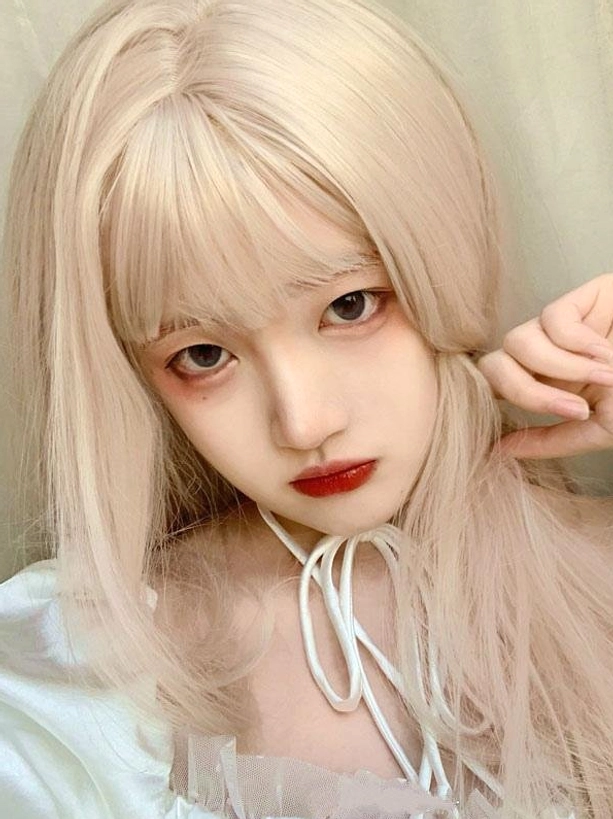 Front close-up portrait of long blonde Lolita wig with blunt bangs on model with red lip makeup and hand posed near face