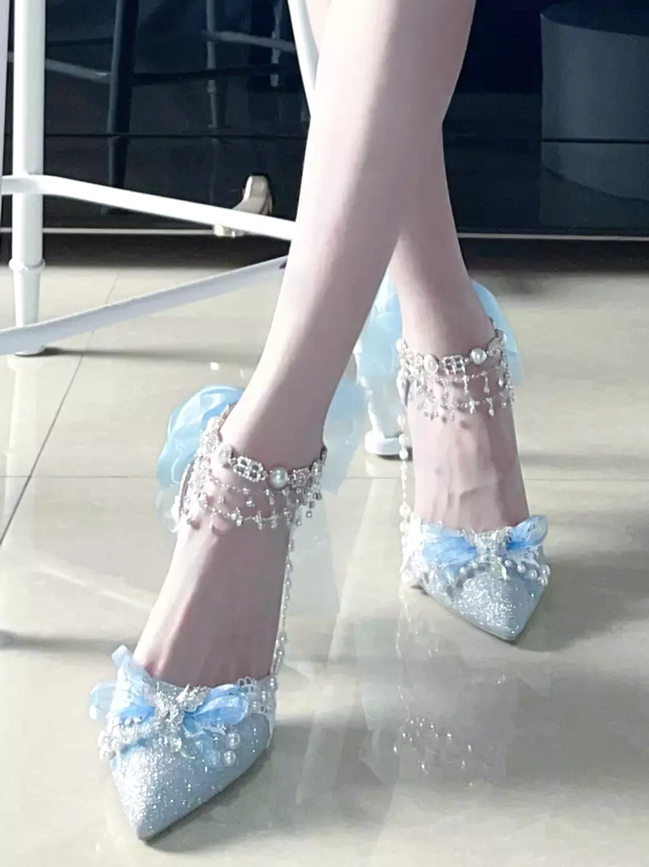 Light blue glitter Lolita stiletto shoe with blue bow and pearl ankle chain on light floor, front close-up view