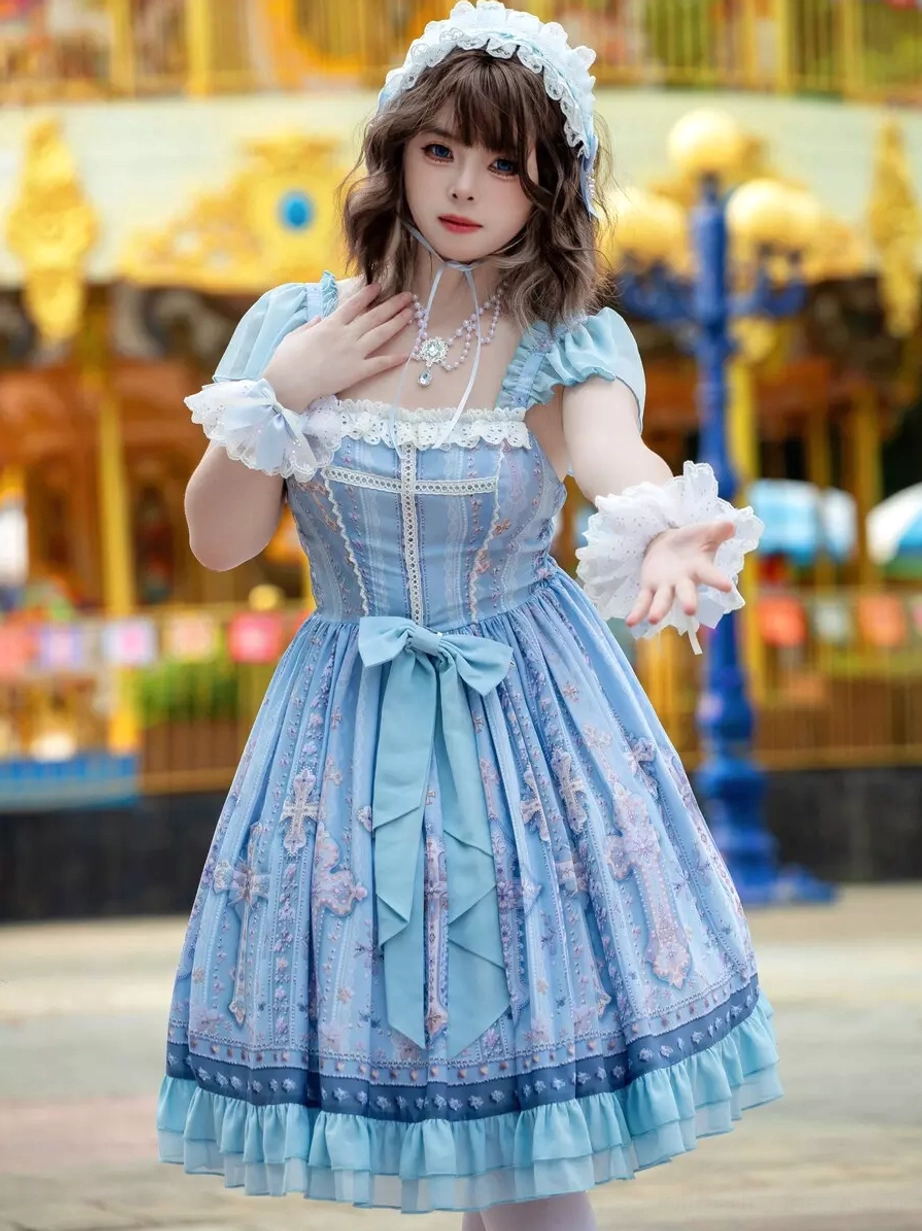 Close-up front view of light blue lolita dress showing detailed lace collar, decorative necklace styling, intricate cross print pattern, and refined embellishment details with blurred carousel background