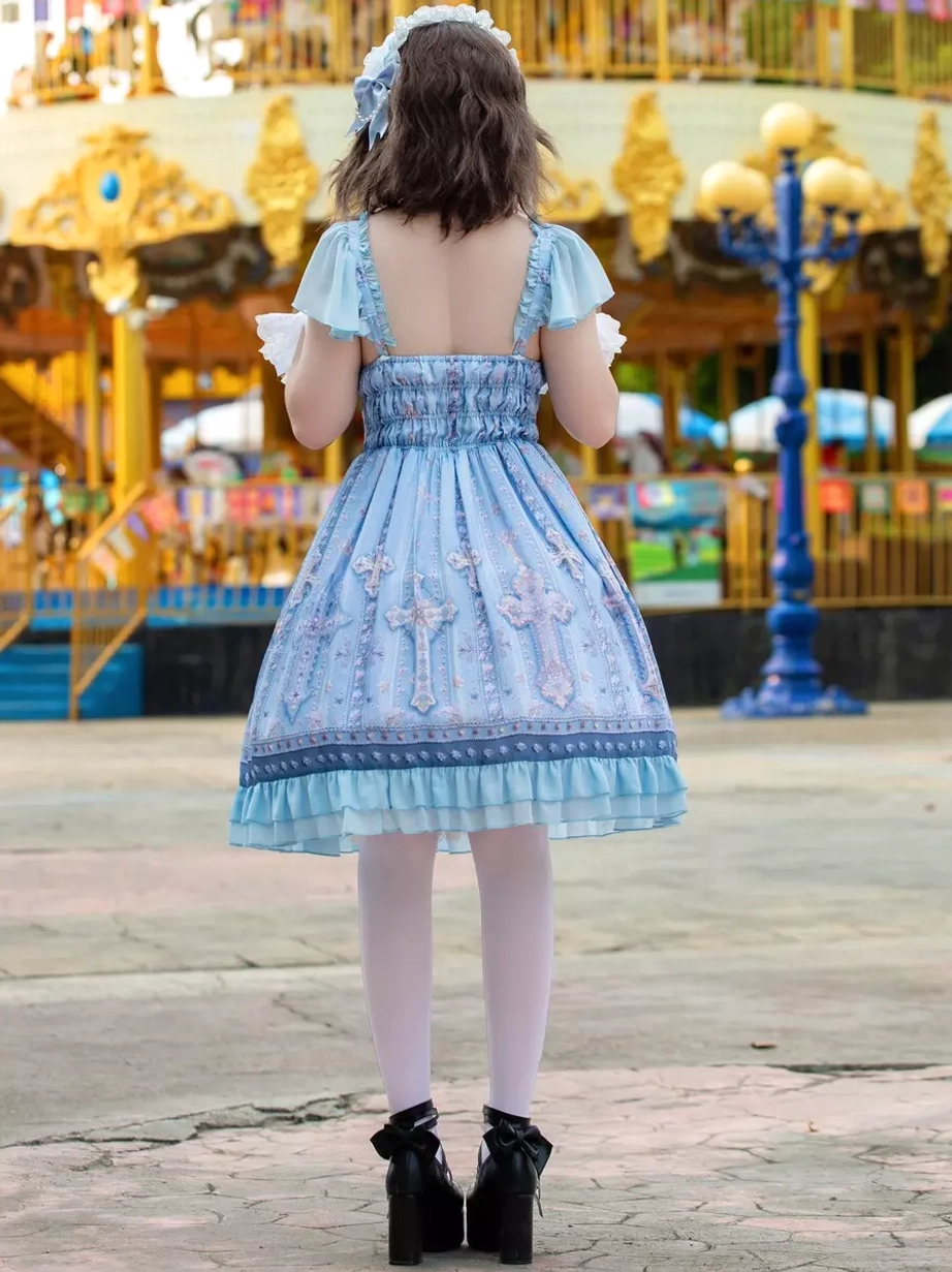 Full back view of light blue lolita JSK dress displaying shirred back bodice, open square back design, ruffled short sleeves, cross pattern print, and structured skirt silhouette at amusement park