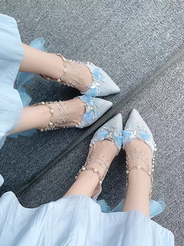 Light blue glitter Lolita shoe with pearl ankle chain, blue bow and stiletto heel on grey carpet, top-down view