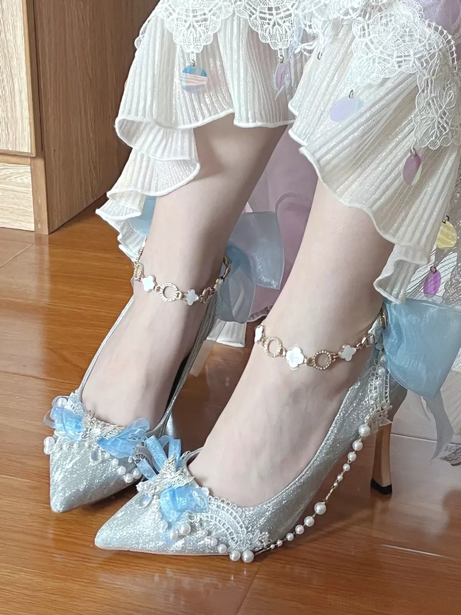 Light blue glitter Lolita stiletto shoe with blue bow and pearl side decorations on wood floor, front close-up view