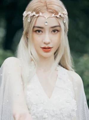 Front close-up portrait of light gold lolita wig featuring straight blonde hair and crystalline leaf tiara against outdoor green background, showing wig construction and color gradient details